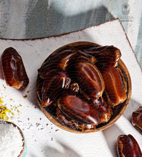 a bowl of sayer dates next to pistachio powder and coconut powder.